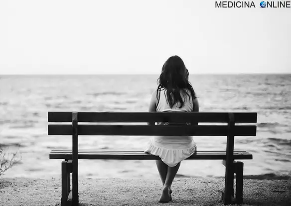 Donna triste e sola seduta su una panchina mentre guarda il mare